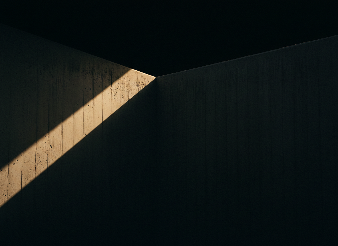 A single narrow shaft of warm golden light cutting diagonally across a dark concrete wall